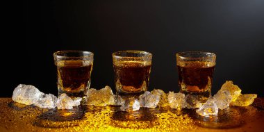Viski ve buz siyah bir masada. Sarı ışık güzel gölgeler yaratır. Boşluğu kopyala.
