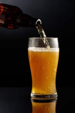 Şişeden bardağa bira dökmek. Siyah yansıtıcı arka planda bir bardak bira..
