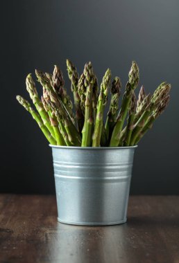 Eski ahşap bir masada küçük kovada taze kuşkonmaz. Boşluğu kopyala.