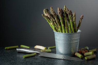 Siyah taş bir masada taze kuşkonmaz ve bıçak. Boşluğu kopyala.