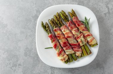 Domuz pastırmasına sarılı ızgara yeşil kuşkonmaz. Gri arka planda beyaz tabakta fotokopi alanı olan ev yapımı atıştırmalıklar. Üst görünüm.