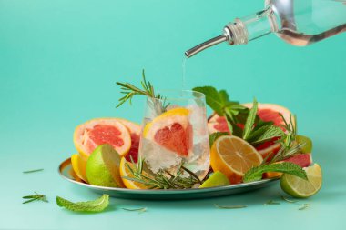 Buzlu, narenciyeli, biberiyeli ve naneli kokteyl. Cin veya rom şişeden bardağa dökülür. Kopyalama alanı olan yeşil arkaplan.