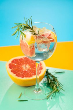 Yaz kokteylini cin, tonik, greyfurt ve biberiyeyle tazeliyorum. Buzda servis ediliyor, renk ve tazelikle dolup taşıyor. Parlak renkli arkaplan.
