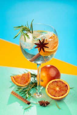 Cin, tonik, kan portakalı, tarçın, anason ve biberiyeli yaz kokteyli. Buzda servis ediliyor, renk ve tazelikle dolup taşıyor. Parlak renkli arkaplan.