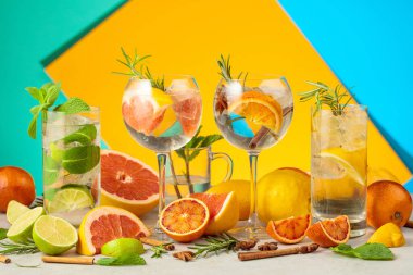 Beyaz mermer bir masada malzemelerle yaz kokteyllerini tazeliyorum. Mojito ve çeşitli cin tonik kokteylleri parlak renkli bir arka planda..