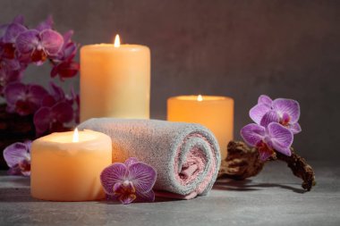 Havlular, orkide çiçekleri ve gri arka planda yanan mumlar. Kopyalama alanı ile kaplıca kavramı.