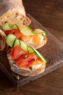 Tütsülenmiş alabalık, krem peynir, taze salatalık ve eski bir kesim tahtasında kapari..