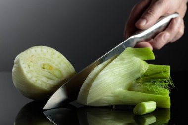 Bıçaklı el ve kesilmiş rezene ampulü. Siyah yansıtıcı arka planda yeşil saplı rezene ampulü.