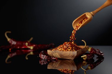 Kuru kırmızı biber ve siyah yansıtıcı arka planda ezilmiş kırmızı biber. Mutfak, baharat ve yemek temaları için boşluk kopyala.