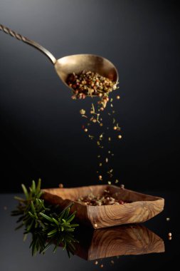 Baharat karışımı ahşap bir kaseye dökülür. Siyah arka planda taze biberiye ve kurutulmuş baharatlar.