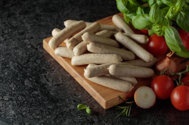 Geleneksel Bavyera beyaz sosisi, fesleğen, soğan, biberiye ve domatesli siyah taş masa. Boşluğu kopyala.