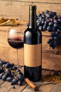 Eski ahşap bir masada bir şişe kırmızı şarap ve mavi üzüm. Eski boş bir şişede. Boşluğu kopyala.