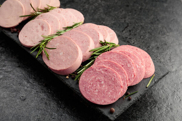 Various boiled sausages with rosemary on a black stone background.