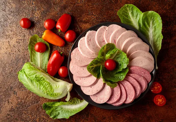 Kahverengi bir arka planda yeşil ve sebzeli çeşitli haşlanmış sosisler..