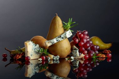 Armut, ceviz, kırmızı üzüm ve biberiyeli mavi peynir. Siyah yansıtıcı arka planda meyveleri olan geleneksel küflü peynir. Boşluğu kopyala.