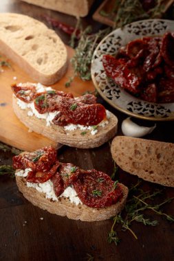 Süzme peynirli ciabatta, kurutulmuş domates ve eski ahşap bir masada kekik. Geleneksel İtalyan atıştırması.