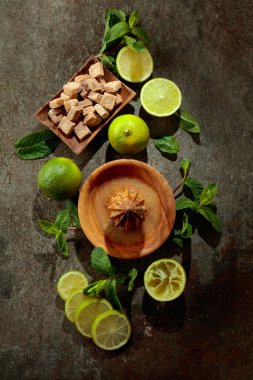 Tahta narenciye sıkacağı ve yaz ferahlatıcı içecekler yapmak için malzemeler. Esmer şeker, limon ve taş bir masada taze nane dalları. Üst görünüm.