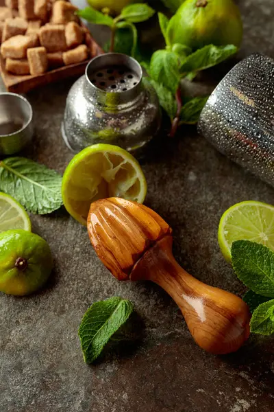 Tahta narenciye sıkacağı, karıştırıcı ve yaz ferahlatıcı içecekler yapmak için malzemeler. Esmer şeker, limon ve taş bir masada taze nane dalları..