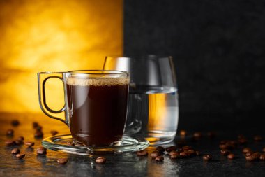 Espresso, bir bardak soğuk su ve siyah taş bir masada kavrulmuş kahve çekirdekleri. Boşluğu kopyala.