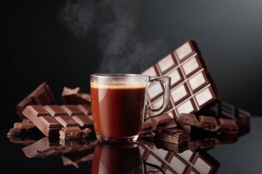 Bir bardak sıcak çikolata ve kırık acı çikolata. Kopyalama alanı olan siyah yansıtıcı arkaplan.