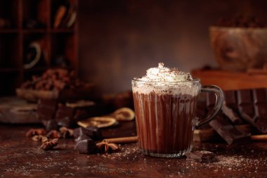 Üzerine krem şanti ve çikolata parçacıkları serpiştirilmiş sıcak çikolata. Eskimiş kahverengi arka planda yer alan malzemeler içeren bir çikolata içeceği..