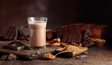 Kahverengi arka planda kremalı sıcak çikolata içeceği. Bir kupa sıcak çikolata, kırık çikolata ve kakao tozu. Boşluğu kopyala.