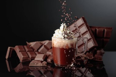 Krem şantili ve çikolata kırıntısı serpiştirilmiş sıcak çikolata. Arka planda kırık bir çikolata parçasında. Siyah yansıtıcı arkaplan.