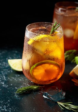 Limonlu buzlu çay, limon ve biberiye dallarıyla süslenmiş buz. Koyu mavi bir masada turunçgil dilimli donmuş bardaklar..