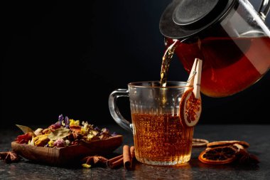 Sıcak bitki çayı cam bardağa dökülür. Kopyalama alanı olan siyah arkaplan.