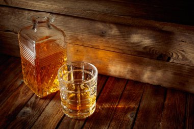 Zarif viski bardağı ve kehribar sıvısıyla dolu sürahi eski bir ahşap masada. Boşluğu kopyala.