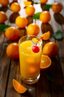Kırmızı kirazla süslenmiş buzlu bir bardak portakal suyu. İçki ve taze meyveler eski ahşap bir masada.
