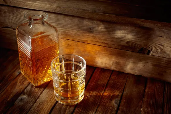 Zarif viski bardağı ve kehribar sıvısıyla dolu sürahi eski bir ahşap masada. Boşluğu kopyala.