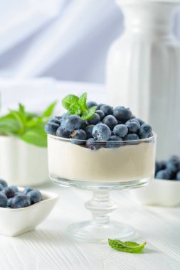 Mascarpone kreması, beyaz ahşap bir masada temiz bir kasede taze yaban mersini. Nane şekeriyle süslenmiş çilekli parfüm..