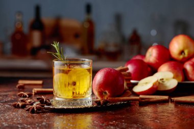 Elma dilimli elma şarabı ve biberiye filizi. Taze elmalar, tarçın çubukları ve anason eski bir mutfak masasına saçılmış..