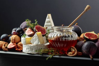 İncirli, üzümlü, cevizli, ballı ve kekikli Camembert peyniri. Siyah arka planda meyveli yumuşak peynir..