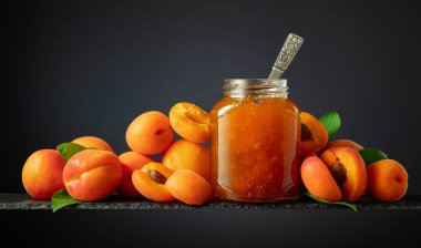 Cam kavanozda kayısı reçeli ve taze meyve. Siyah arka planda güzel bir kesişme. Boşluğu kopyala.