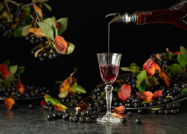 Siyah böğürtlen likörü ve siyah taş bir masada taze böğürtlen. Tatlı aromalı içecek şişeden bardağa dökülür..