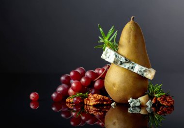 Armutlu mavi peynir, ceviz, kırmızı üzüm ve siyah arka planda biberiye. Siyah yansıtıcı arka planda meyveleri olan geleneksel küflü peynir. Boşluğu kopyala.