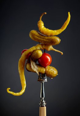 Çatalın üzerinde sebze turşusu. Siyah arka planda konserve sarı biber, salatalık ve domates..