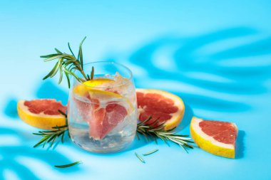 Buzlu, pembe greyfurtlu ve biberiyeli yaz ferahlatıcı içecek. Kopyalama alanı olan mavi arkaplan.