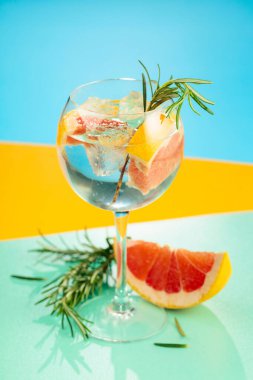 Yaz kokteylini cin, tonik, greyfurt ve biberiyeyle tazeliyorum. Buzda servis ediliyor, renk ve tazelikle dolup taşıyor. Parlak renkli arkaplan.