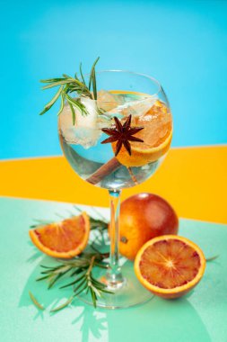 Cin, tonik, kan portakalı, tarçın, anason ve biberiyeli yaz kokteyli. Buzda servis ediliyor, renk ve tazelikle dolup taşıyor. Parlak renkli arkaplan.