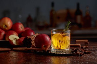 Elma dilimleri ve biberiye filizi ile elmalı kombu çayı. Taze elmalar, tarçın çubukları ve anason eski bir mutfak masasına saçılmış..