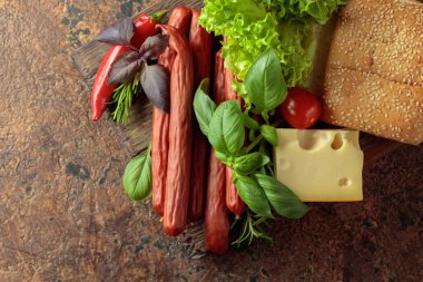 İnce tütsülenmiş sosis, peynir, ekmek ve sebzeler eski bir kesim tahtasının üzerinde. Üst görünüm, alanı kopyala.