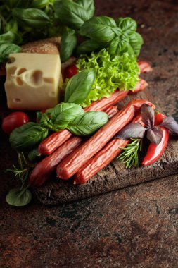 İnce tütsülenmiş sosisler peynir, ekmek ve yeşillikler eski bir kesim tahtasında.