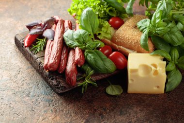 İnce tütsülenmiş sosisler peynir, ekmek ve yeşillikler eski bir kesim tahtasında.