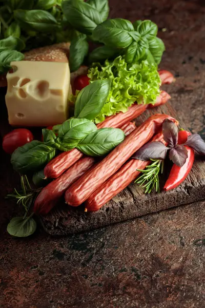 İnce tütsülenmiş sosisler peynir, ekmek ve yeşillikler eski bir kesim tahtasında.