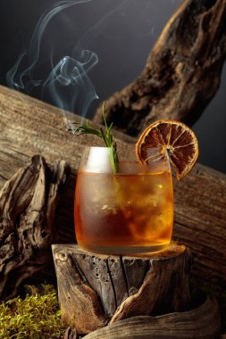 Eski usul bir kokteyl, buzlu, tahta bir kütükte. Kurutulmuş portakal dilimi ve yanan biberiye filizi ile süslenmiş soğuk, ferahlatıcı bir içecek..