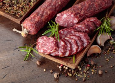 Ahşap bir masada baharat ve otlarla dilimlenmiş füme sosis..