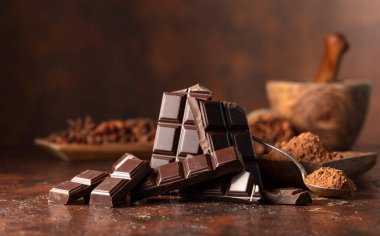 Kahverengi bir masada kırılmış siyah çikolata ve kakao tozu. Boşluğu kopyala.